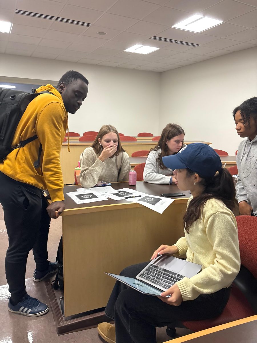 Members gathered around a desk reviewing project designs on paper and a laptop