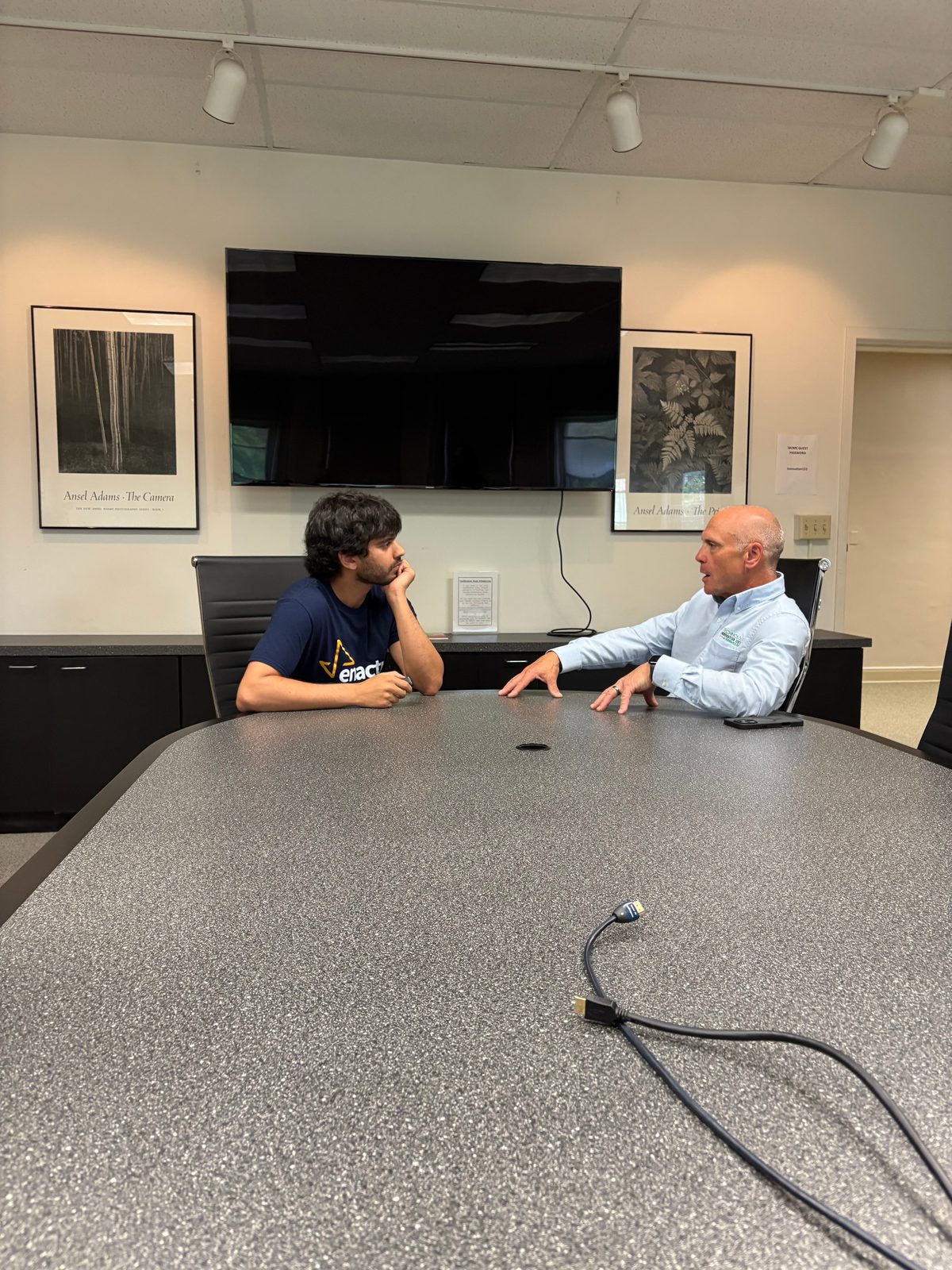 A member in an Enactus shirt listening to a community partner across a conference table