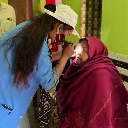 A screener in a blue coat shining a light into an older woman's eye during an eye exam